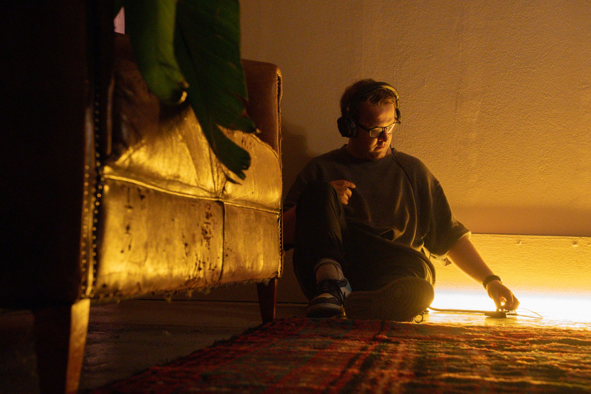 Naulé on the floor in headphones, lit by a warm amber light