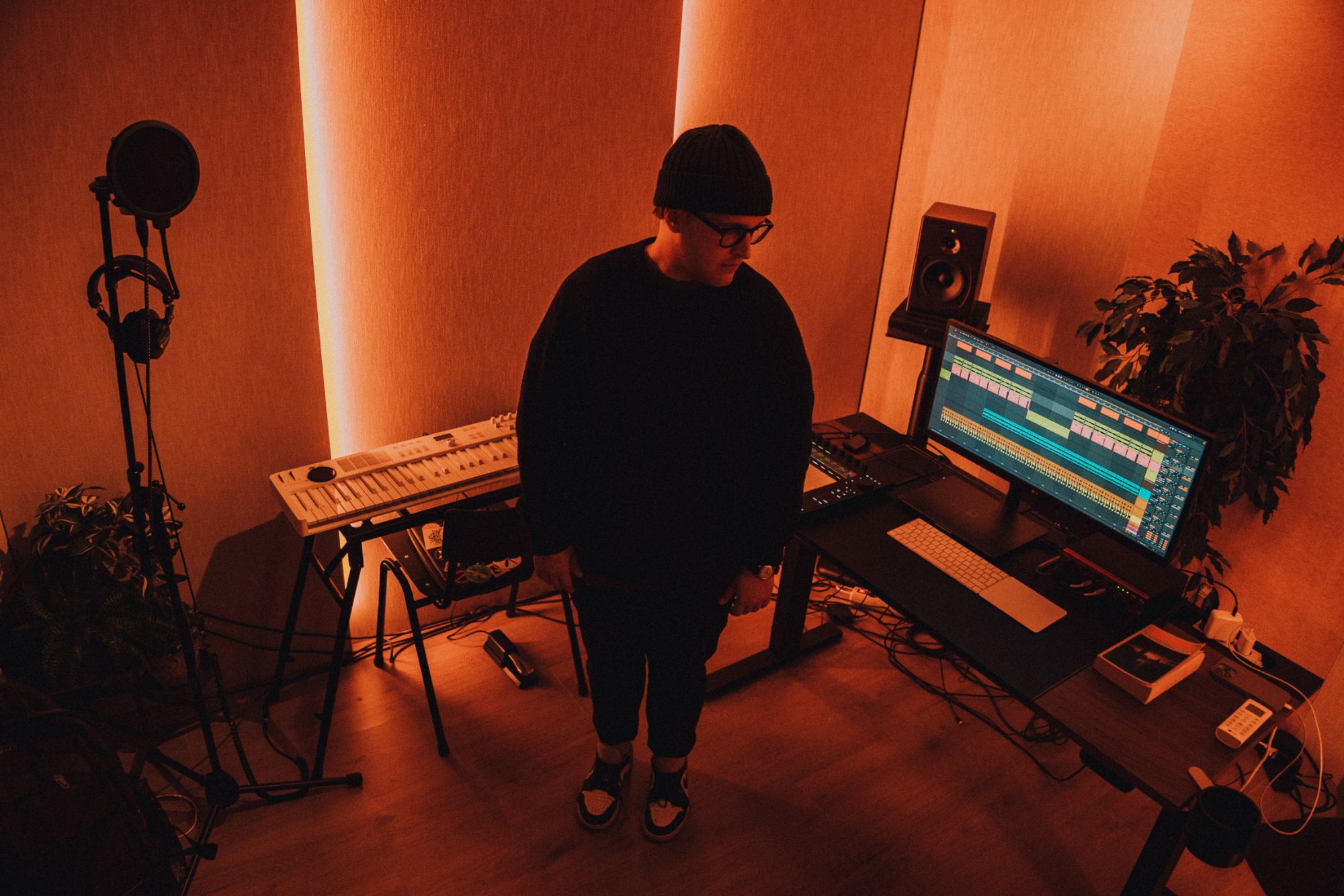 Naulé standing in his studio between a keyboard and his desk, in deep orange light